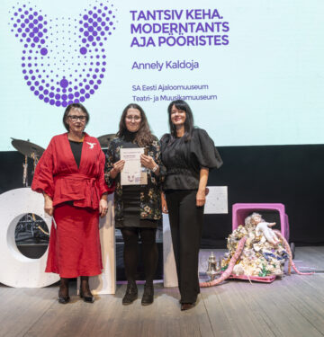 Pildil seisavad Sirje Helme, Annely Kaldoja ja Heidy Purga kõrvuti laval, Kaldoja hoiab käes heledat diplomit. Nende selja taga ekraanil on kirjas "TANTSIV KEHA. MODERNTANTS AJA PÖÖRISTES" / Annely Kaldoja / SA Eesti Ajaloomuuseum / Teatri- ja Muusikamuuseum".