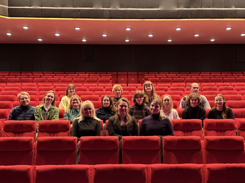 Pildil on 15 inimest, kes istuvad Ugala Teatri suures saalis punastel publikutoolidel.