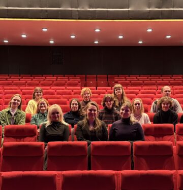 Pildil on 15 inimest, kes istuvad Ugala Teatri suures saalis punastel publikutoolidel.